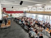 Roman Höllbacher (Künstlerischer Leiter Initiative Architektur) spricht vor Schüler*innen der HTL Saalfelden zur Abwicklung und Vergabe des Architekturpreis Land Salzburg.